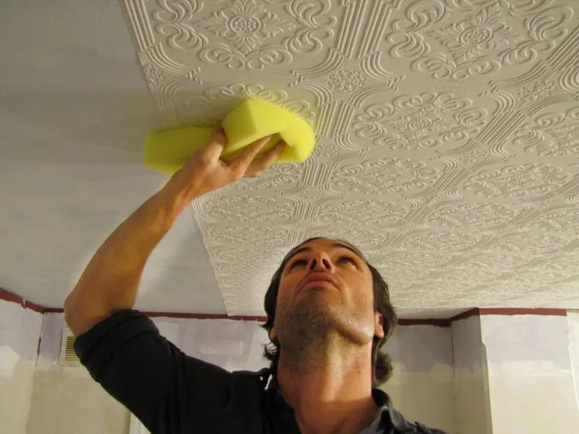 Мужчина пытается оттереть потолок из полистирольных плит